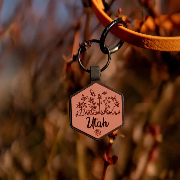 Hexagonal keychain with 'Utah' text and floral design on a blurred natural background